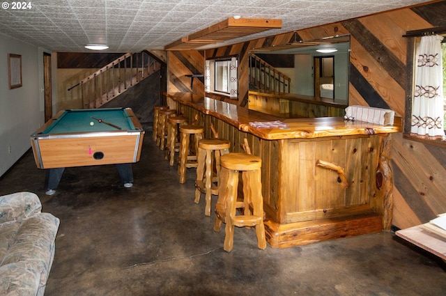 bar featuring stairway, wood walls, a bar, and finished concrete floors