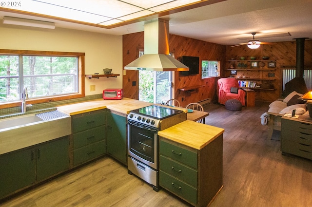 kitchen featuring butcher block countertops, island exhaust hood, stainless steel range with electric cooktop, green cabinetry, and a wood stove