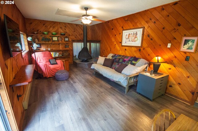 living room with dark wood-type flooring, a wood stove, wood walls, and ceiling fan