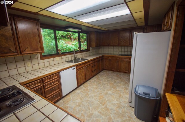 kitchen featuring white appliances, backsplash, sink, and tile counters