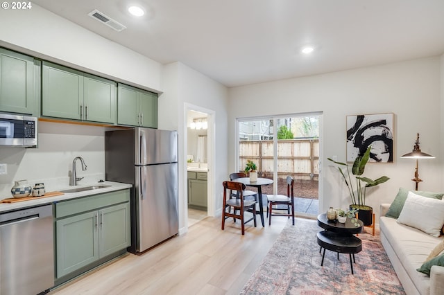 kitchen with green cabinetry, appliances with stainless steel finishes, sink, and light hardwood / wood-style flooring