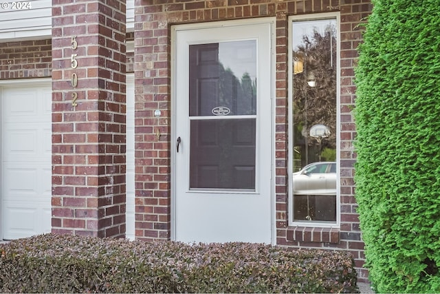 entrance to property featuring a garage and brick siding