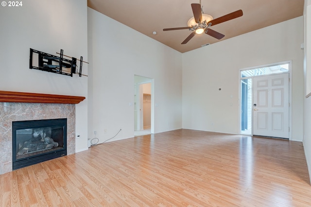 unfurnished living room featuring a premium fireplace, light hardwood / wood-style flooring, and a high ceiling