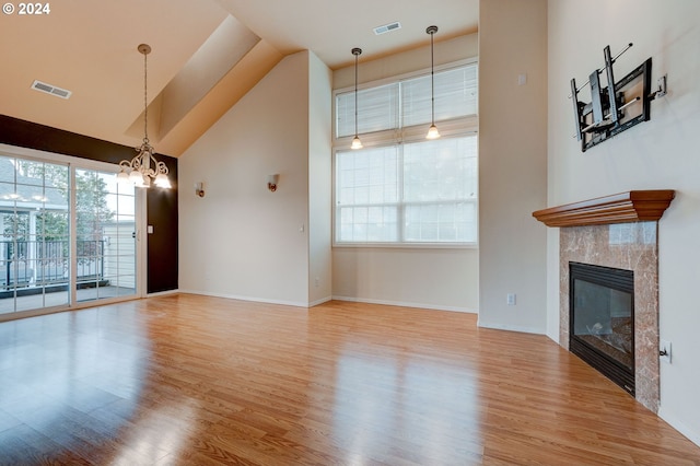 unfurnished living room with a high end fireplace, wood-type flooring, high vaulted ceiling, and a notable chandelier