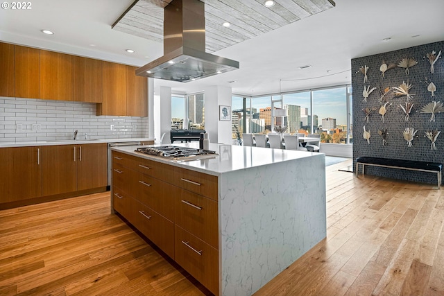 kitchen featuring range hood, a kitchen island, light hardwood / wood-style floors, stainless steel gas cooktop, and sink