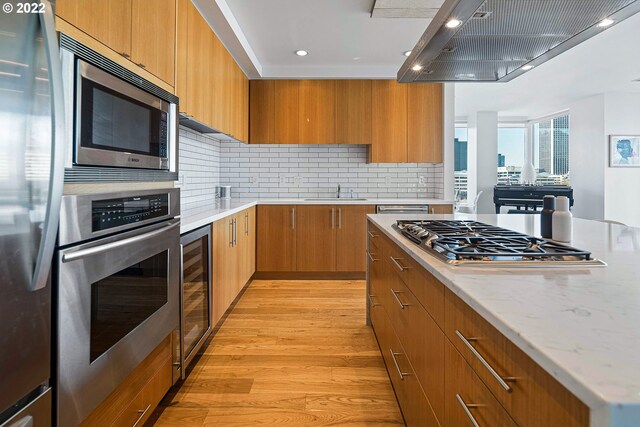 kitchen with beverage cooler, decorative backsplash, appliances with stainless steel finishes, island exhaust hood, and light hardwood / wood-style floors