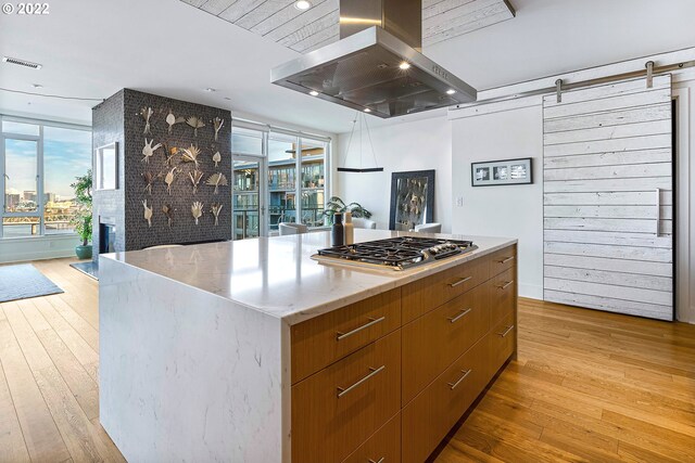 kitchen featuring light wood-type flooring, island exhaust hood, a barn door, a kitchen island, and stainless steel gas stovetop