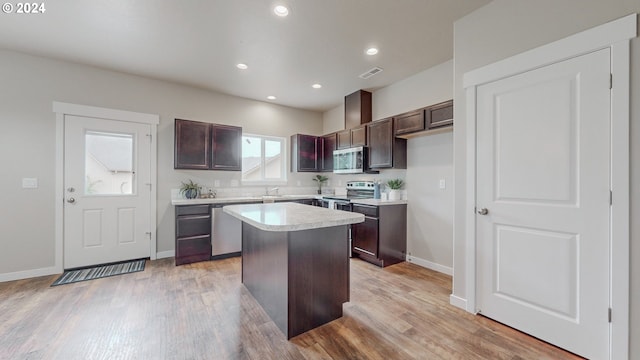 kitchen with appliances with stainless steel finishes, dark brown cabinetry, a kitchen island, and light wood-type flooring