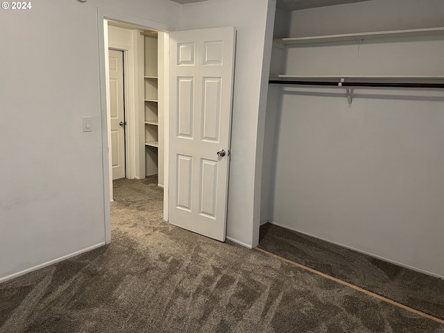 unfurnished bedroom with dark carpet and a closet