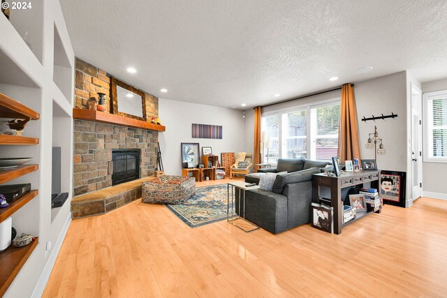 living room with a textured ceiling, hardwood / wood-style floors, and a stone fireplace