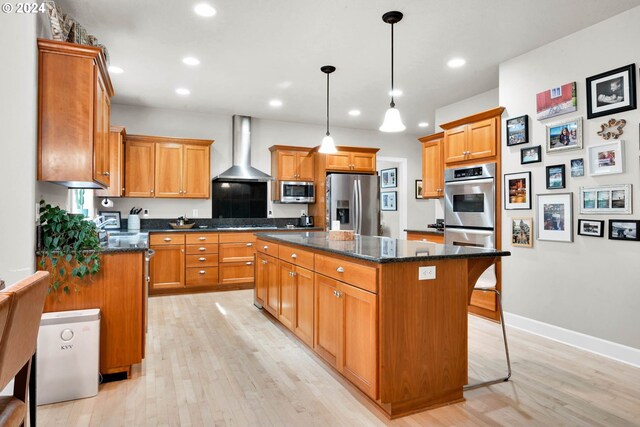 kitchen featuring wall chimney range hood, a center island, stainless steel appliances, and light wood-type flooring