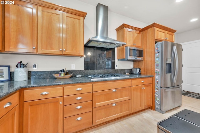 kitchen with light wood-type flooring, dark stone countertops, stainless steel appliances, and wall chimney exhaust hood