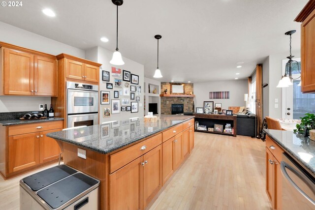 kitchen featuring a fireplace, pendant lighting, stainless steel appliances, a center island, and light hardwood / wood-style floors