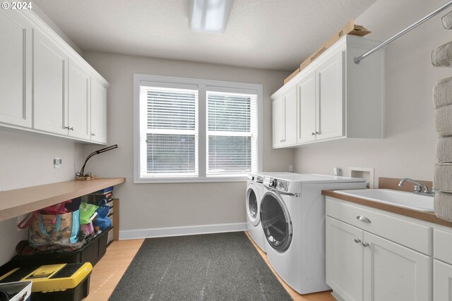 laundry room featuring cabinets, washer and clothes dryer, sink, and light hardwood / wood-style flooring