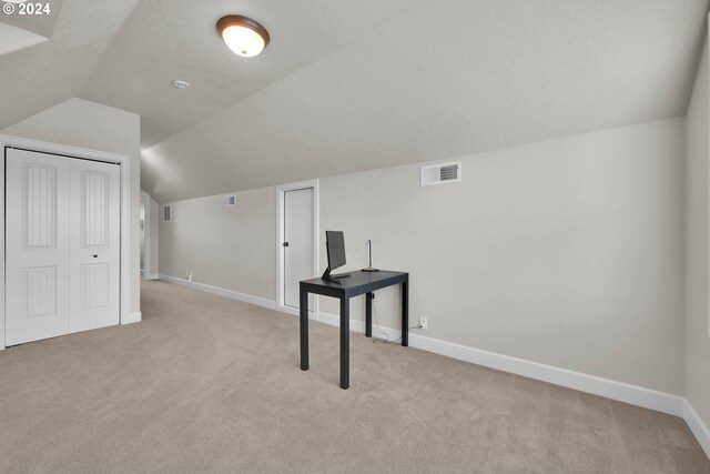 bonus room with lofted ceiling, light carpet, and a textured ceiling