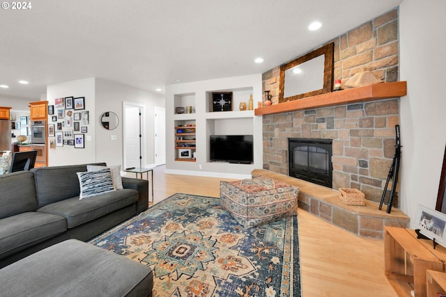 living area with a stone fireplace, built in features, recessed lighting, and light wood-type flooring