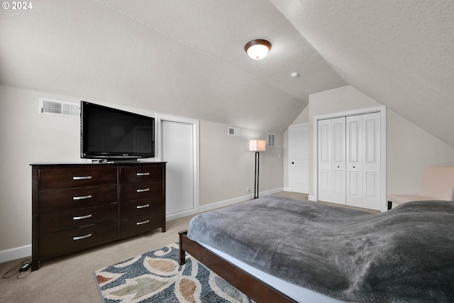 bedroom with lofted ceiling, a closet, light colored carpet, and a textured ceiling