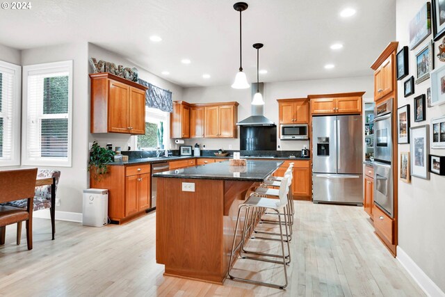 kitchen featuring hanging light fixtures, appliances with stainless steel finishes, light hardwood / wood-style floors, dark stone counters, and a kitchen island