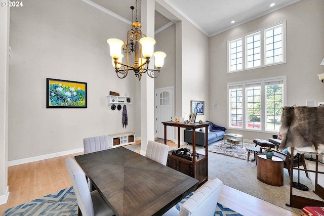 dining space featuring ornamental molding, a high ceiling, a notable chandelier, and light wood-type flooring