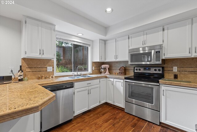 kitchen featuring stainless steel appliances, dark wood-type flooring, sink, white cabinetry, and backsplash