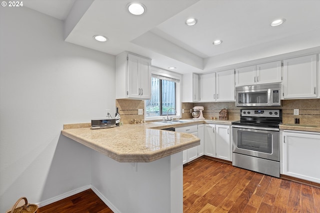 kitchen featuring tasteful backsplash, dark hardwood / wood-style flooring, kitchen peninsula, appliances with stainless steel finishes, and white cabinetry