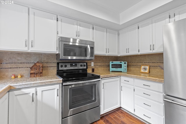 kitchen featuring wood-type flooring, decorative backsplash, stainless steel appliances, and white cabinets