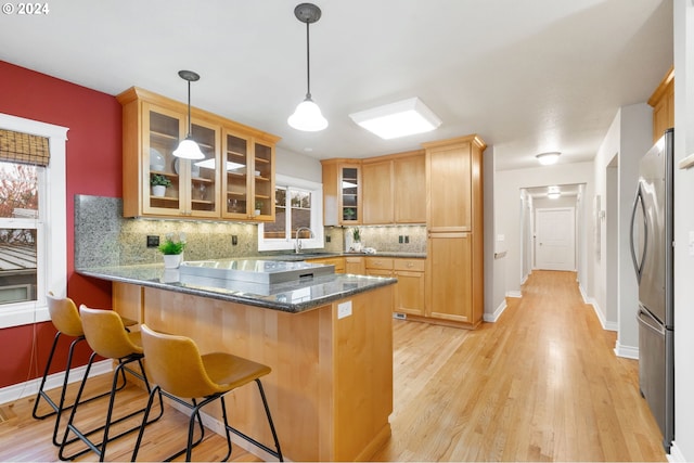 kitchen with a breakfast bar area, kitchen peninsula, a healthy amount of sunlight, and light hardwood / wood-style floors