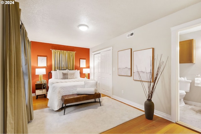 bedroom with light hardwood / wood-style floors, a textured ceiling, connected bathroom, and a closet