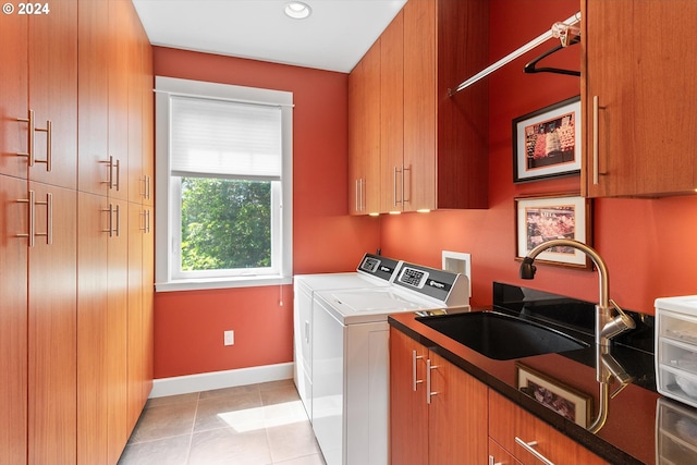 clothes washing area featuring washing machine and dryer, cabinet space, a sink, light tile patterned floors, and baseboards