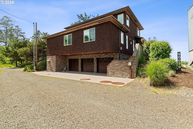 view of side of home with an attached garage, stone siding, and concrete driveway