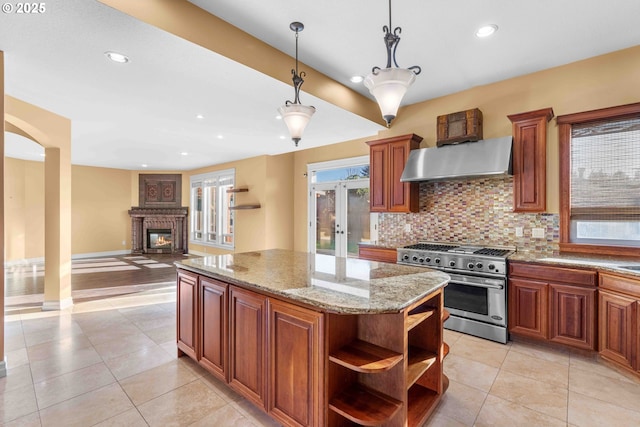 kitchen featuring light stone countertops, high end stove, a large fireplace, decorative light fixtures, and range hood