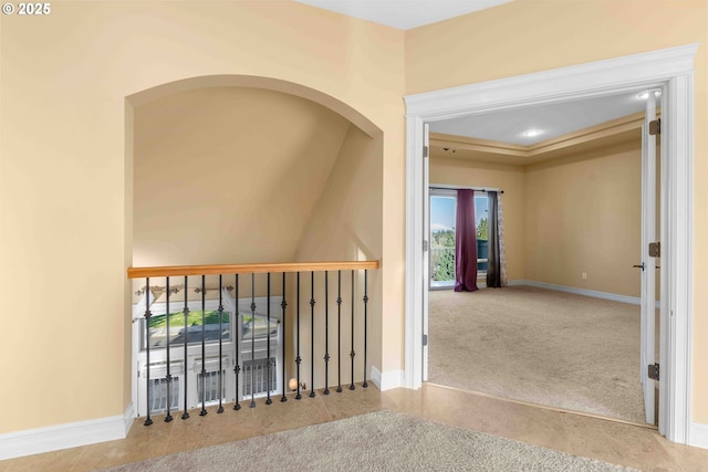 hallway with a tray ceiling and light colored carpet