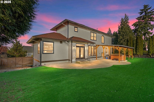 back house at dusk with a patio area, a yard, and a hot tub