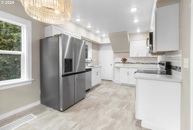 kitchen with white cabinets, stainless steel appliances, decorative backsplash, sink, and a chandelier