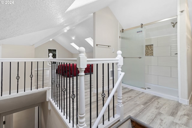 staircase featuring a textured ceiling, vaulted ceiling with skylight, and wood-type flooring