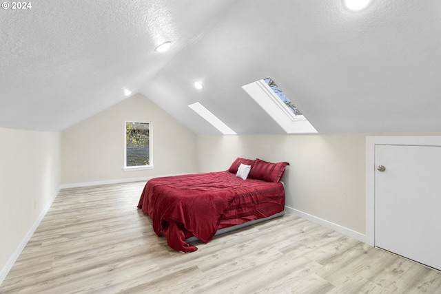 bedroom featuring vaulted ceiling with skylight, a textured ceiling, and light hardwood / wood-style floors