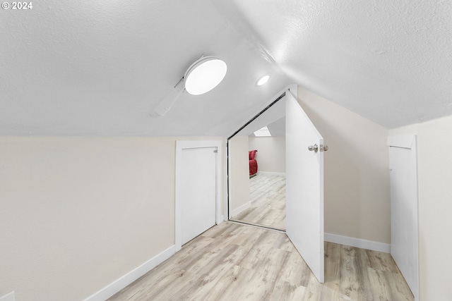 additional living space with vaulted ceiling, a textured ceiling, and light hardwood / wood-style flooring