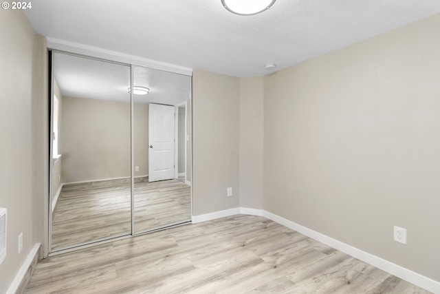 unfurnished bedroom with light wood-type flooring, a closet, and a textured ceiling