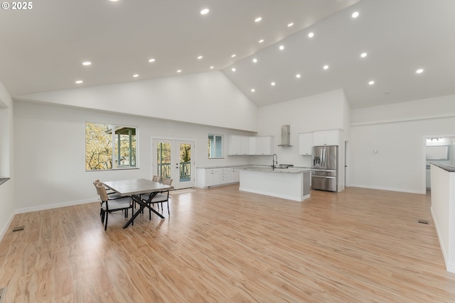 interior space with a center island with sink, stainless steel refrigerator with ice dispenser, light hardwood / wood-style floors, light stone counters, and white cabinetry