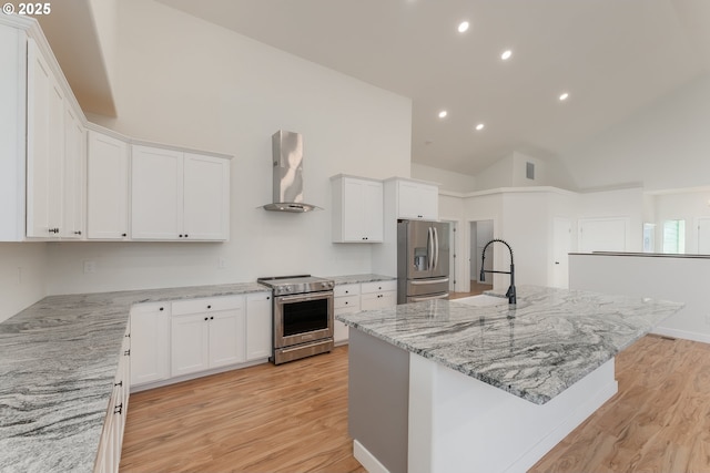 kitchen featuring wall chimney exhaust hood, light stone counters, an island with sink, white cabinets, and appliances with stainless steel finishes