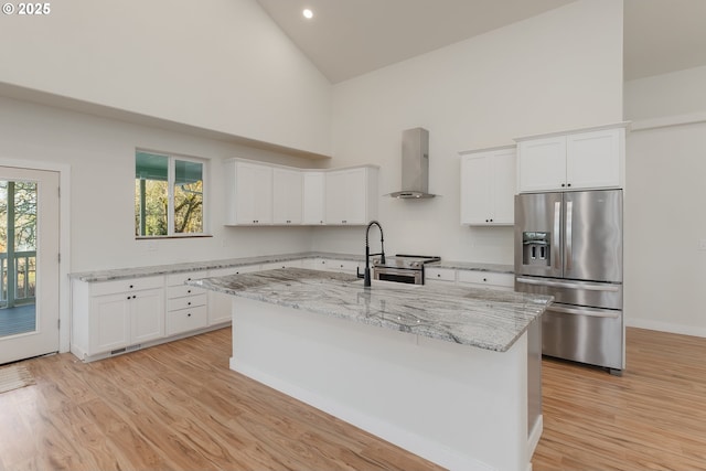 kitchen featuring a center island with sink, white cabinets, stainless steel appliances, and wall chimney range hood