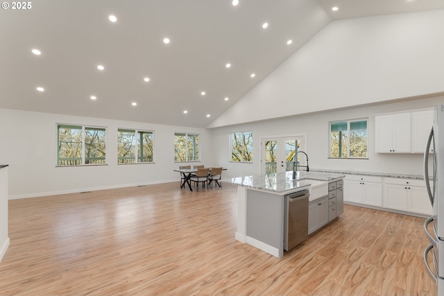 kitchen featuring light stone countertops, stainless steel appliances, light hardwood / wood-style flooring, white cabinetry, and an island with sink