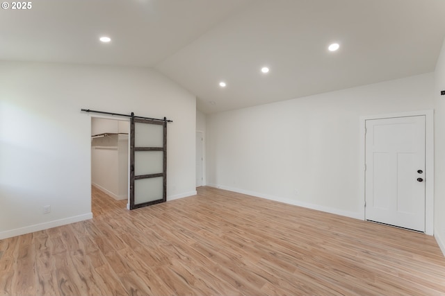 unfurnished bedroom featuring a barn door, light hardwood / wood-style flooring, a closet, and lofted ceiling