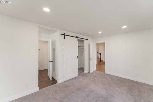 unfurnished bedroom with a walk in closet, a barn door, carpet floors, and a closet