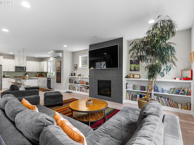 living room with sink, light hardwood / wood-style flooring, a wall mounted AC, and a tile fireplace