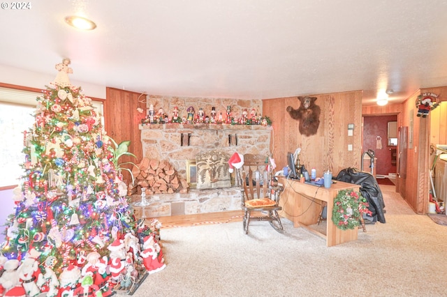 carpeted living area with a stone fireplace and wood walls