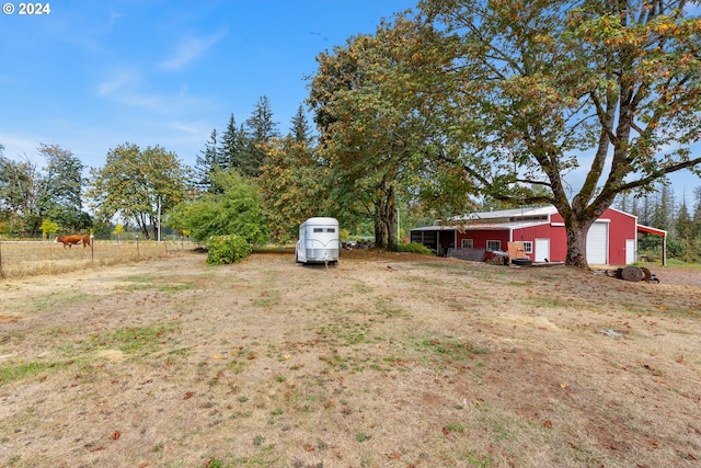 view of yard featuring a garage, a rural view, and an outbuilding