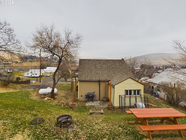 back of property featuring a lawn, a mountain view, and an outdoor fire pit