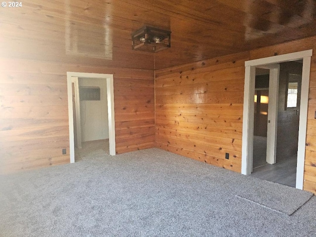 unfurnished room featuring carpet flooring, wood walls, and wooden ceiling