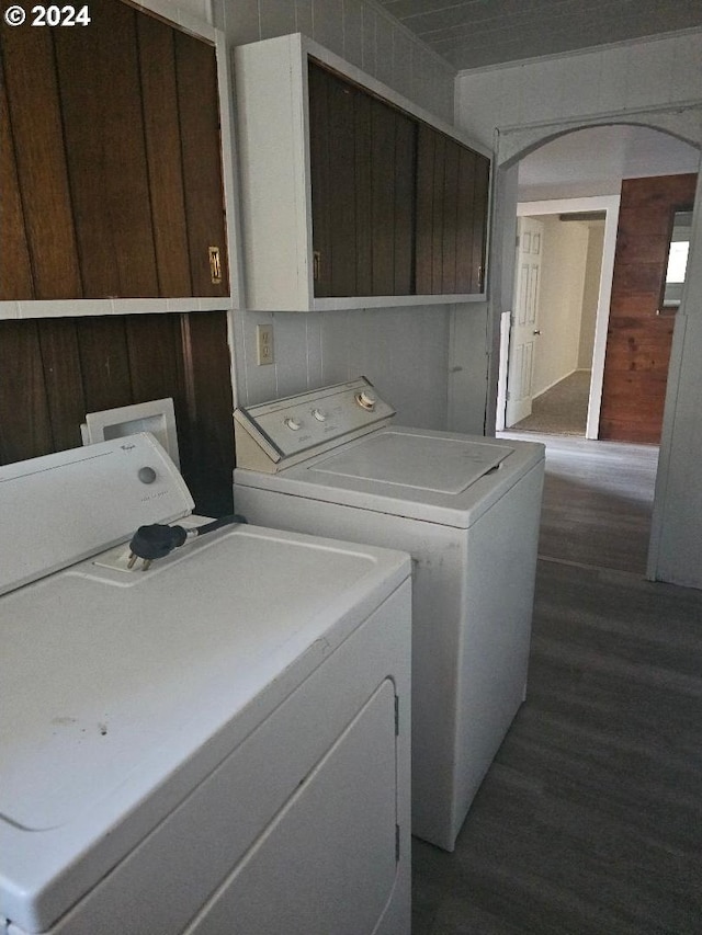 clothes washing area with cabinets, dark hardwood / wood-style flooring, washer and clothes dryer, and wood walls